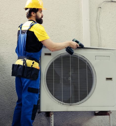 Professional technician starting work on faulty air conditioner, using power drill to disassemble condenser metal coil panel. Expert engineer dismantling hvac system to check for leaks